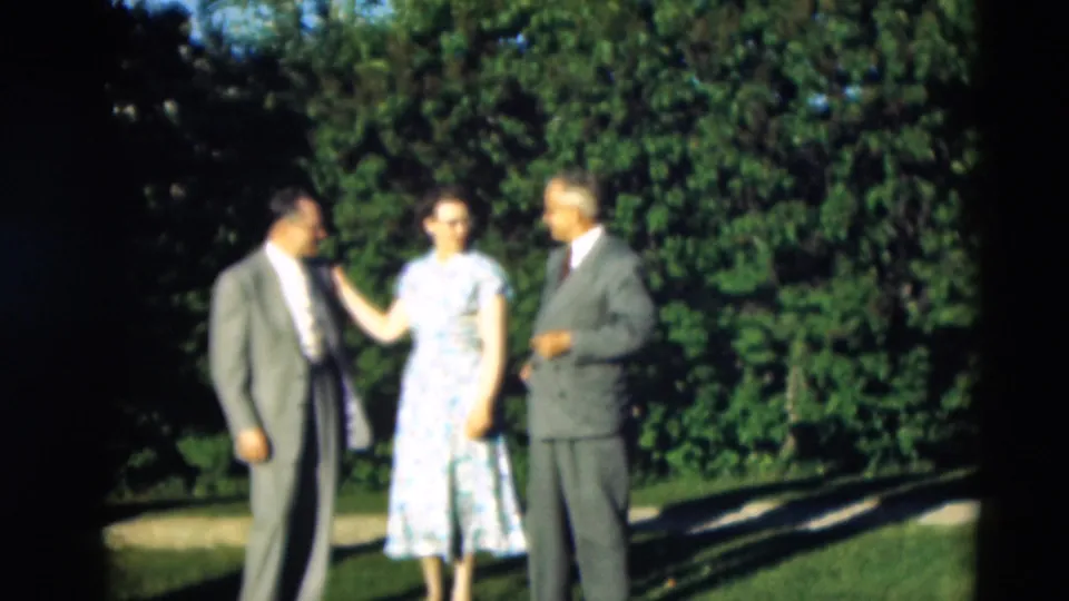 In 1951 Paducah home-movie footage, a woman in a light blue floral dress stands between two suited men on a sunny lawn.