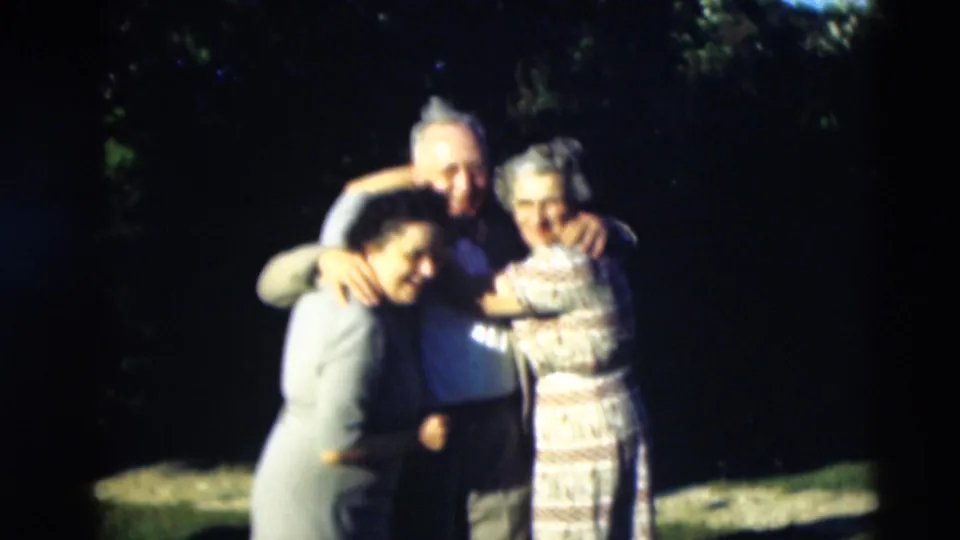 1951 Paducah home-movie frame showing three adults smiling and embracing together in a garden setting.