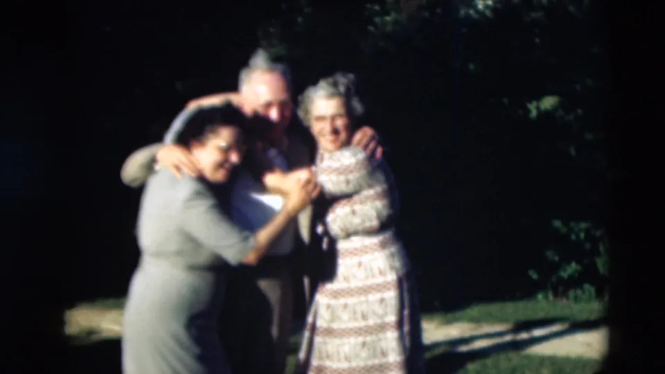 Three adults in 1951 Paducah home-movie footage stand close together outdoors, smiling and holding each other near trees and grass.