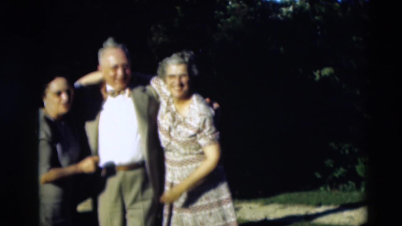 A man stands between two women as they hold his arms outdoors.