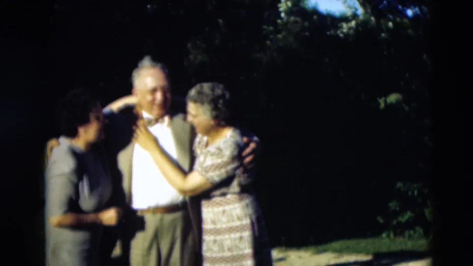 Two women and a man in 1951 home-movie footage remain close together outdoors, with one woman turned toward him in bright sunlight.