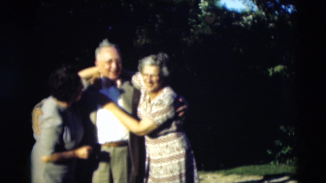 Three adults hug outdoors while another woman stands nearby in bright sunlight.