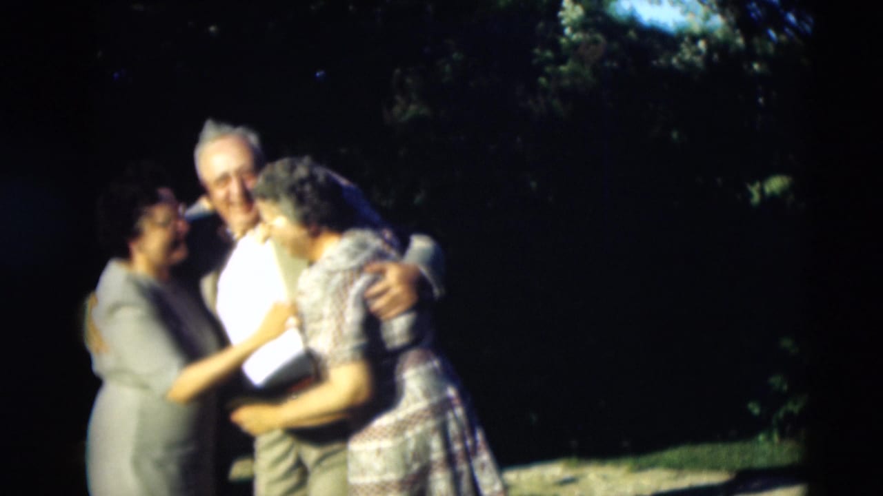 A man in a light shirt and jacket embraces two women in an outdoor 1951 Paducah scene, with trees behind them.