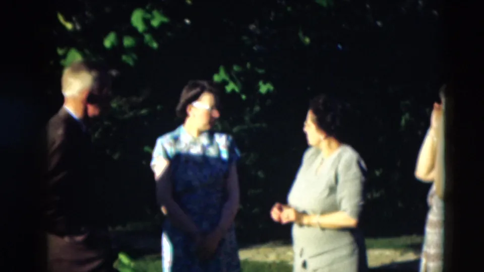 Several adults stand and converse outdoors in the Paducah 1951 home movie, with a woman in a blue floral dress near the center.