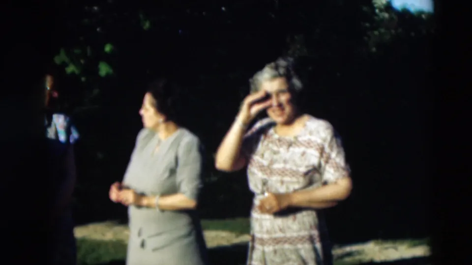 1951 Paducah home-movie frame with two women in dresses centered under trees and a third woman partly visible at frame edge.