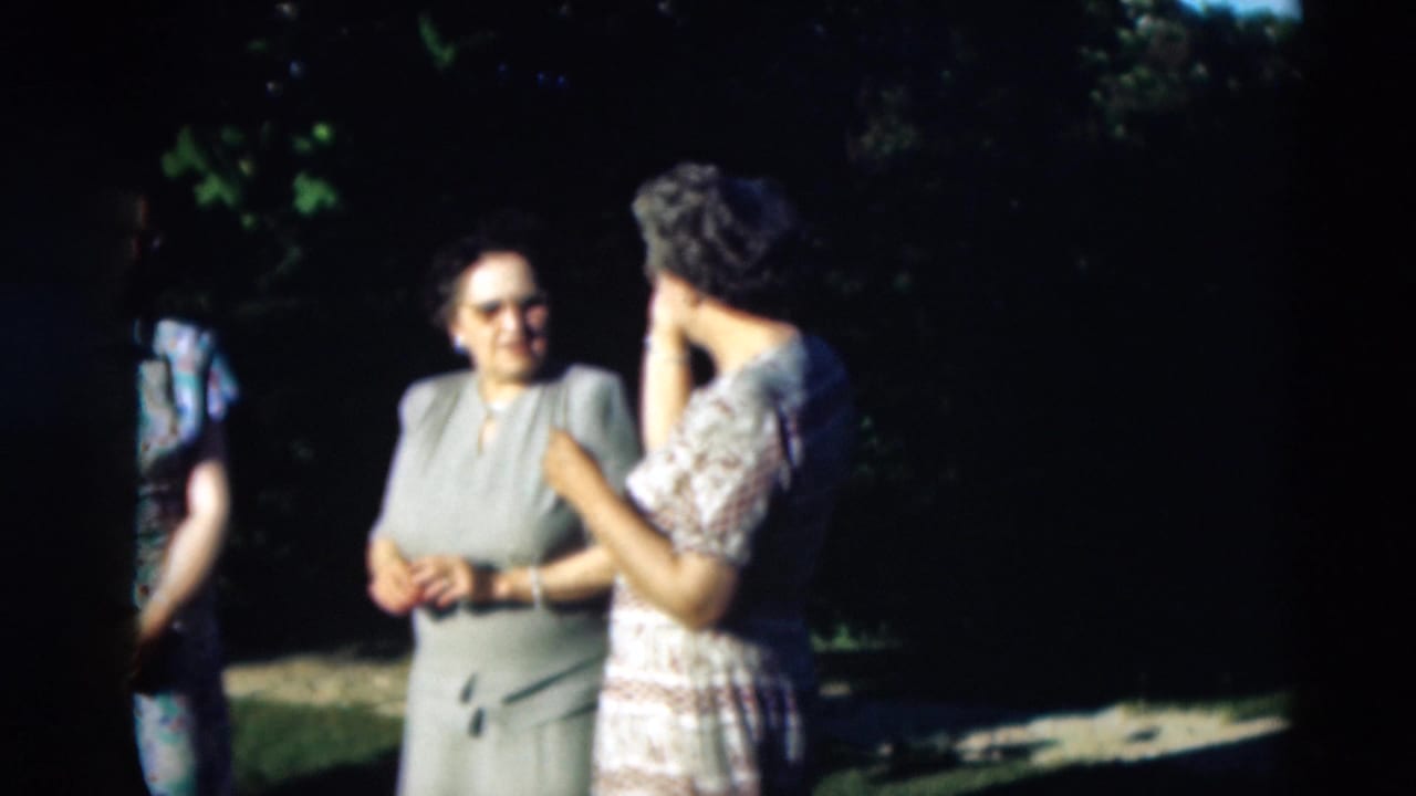 Two women stand talking outdoors, with another person partly visible at the edge.