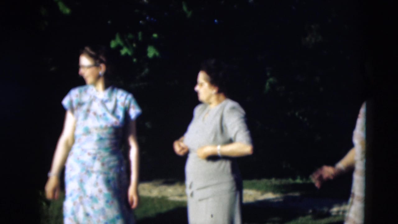Two women stand apart outdoors in sunlight and shade.