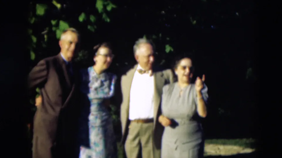 Four adults face the camera in a 1951 Paducah, Kentucky outdoor home-movie scene, framed by dark foliage and sunlight.