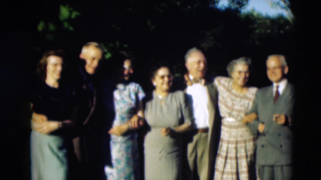 1951 Paducah home-movie frame showing adults in dresses and suits standing arm in arm outdoors under trees.