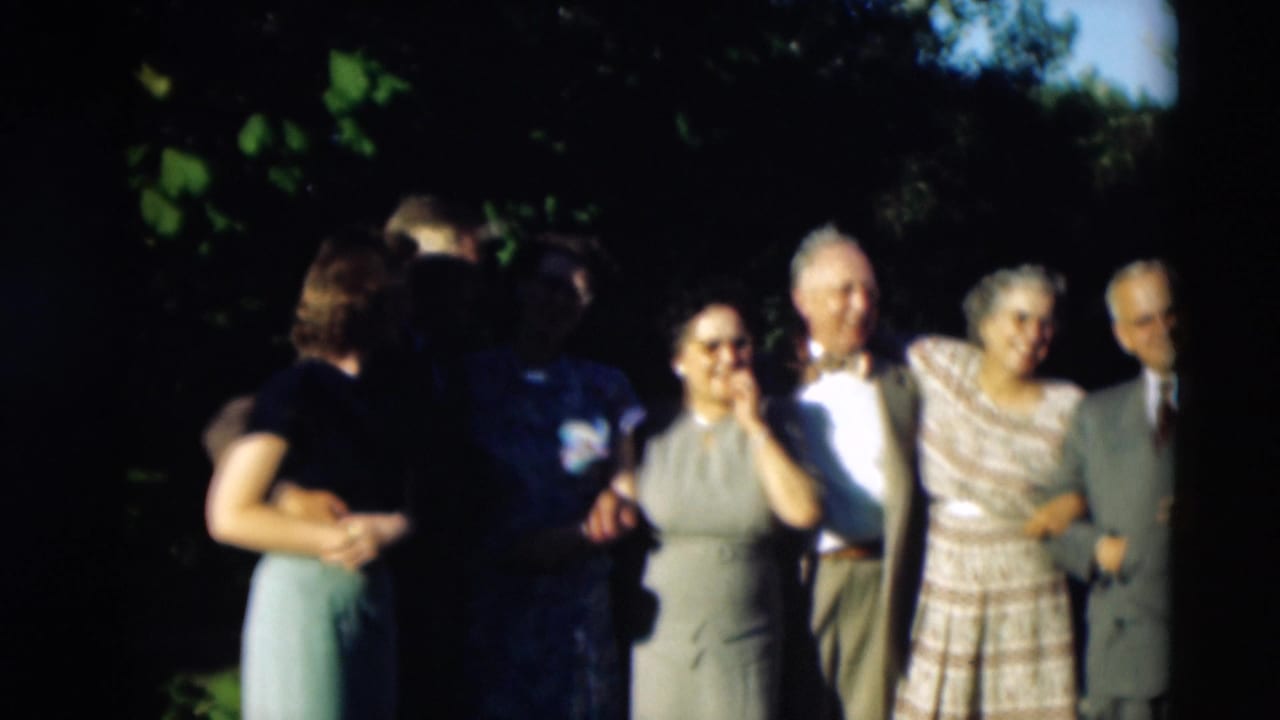 Adults at the Paducah family gathering stand in bright sun and shade while two people face each other near the camera.