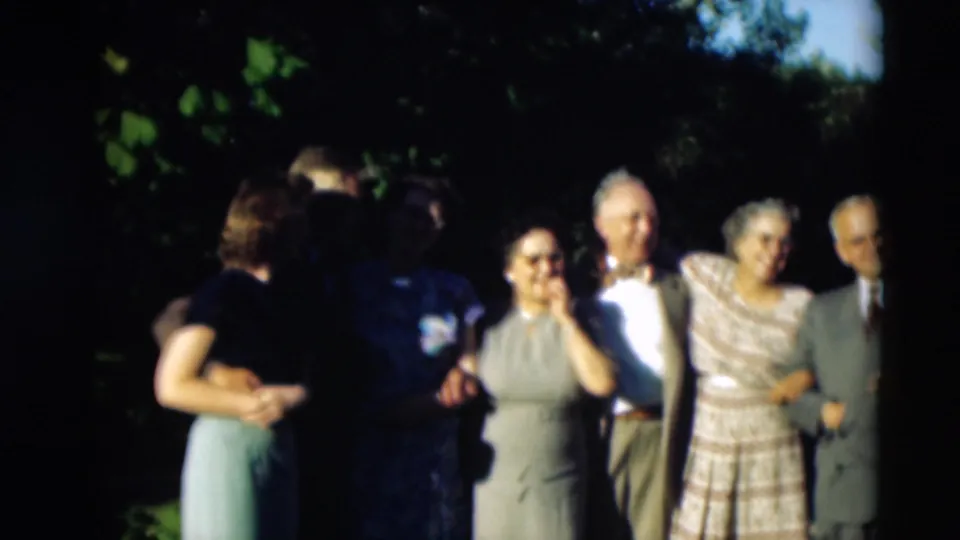 Adults at the Paducah family gathering stand in bright sun and shade while two people face each other near the camera.