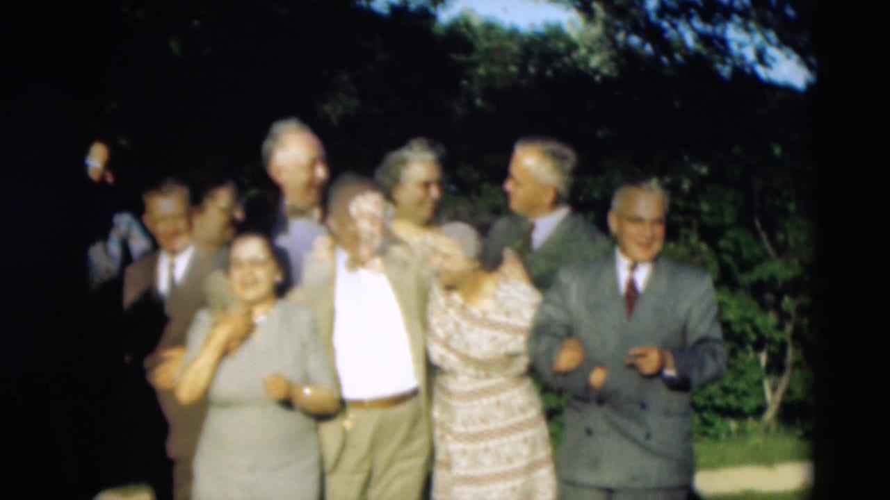 In supplied 1951 Paducah home-movie footage, older friends stand close together outdoors, smiling and linking arms near trees.