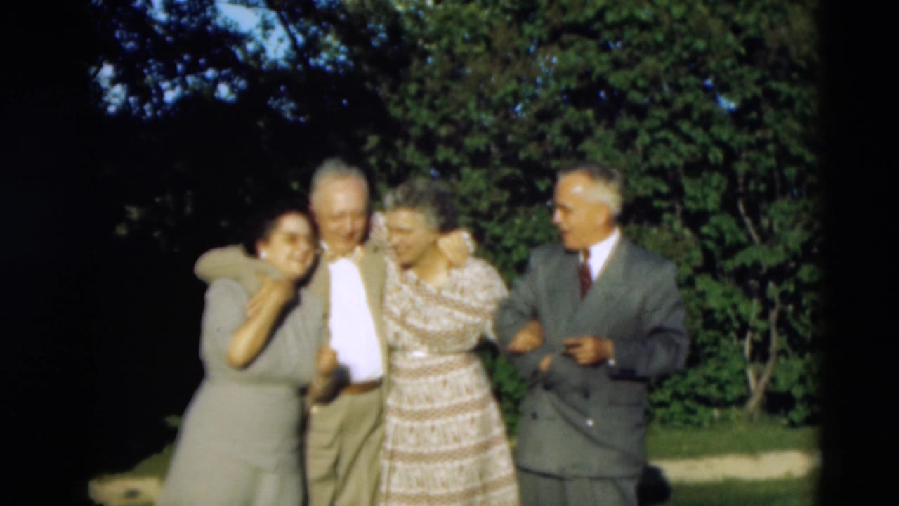 Four older adults lean together outdoors, smiling toward the camera.