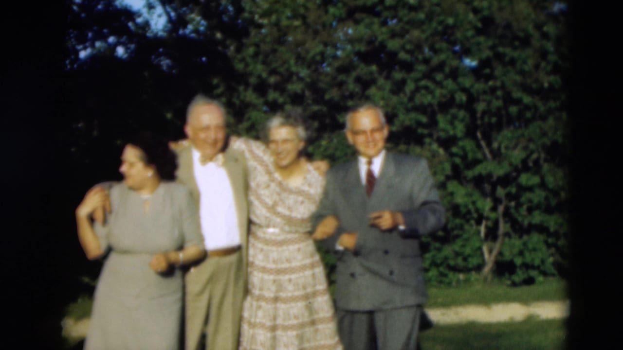 Four elderly adults in formal clothing smile and hold arms in a sunlit Paducah outdoor scene from 1951.