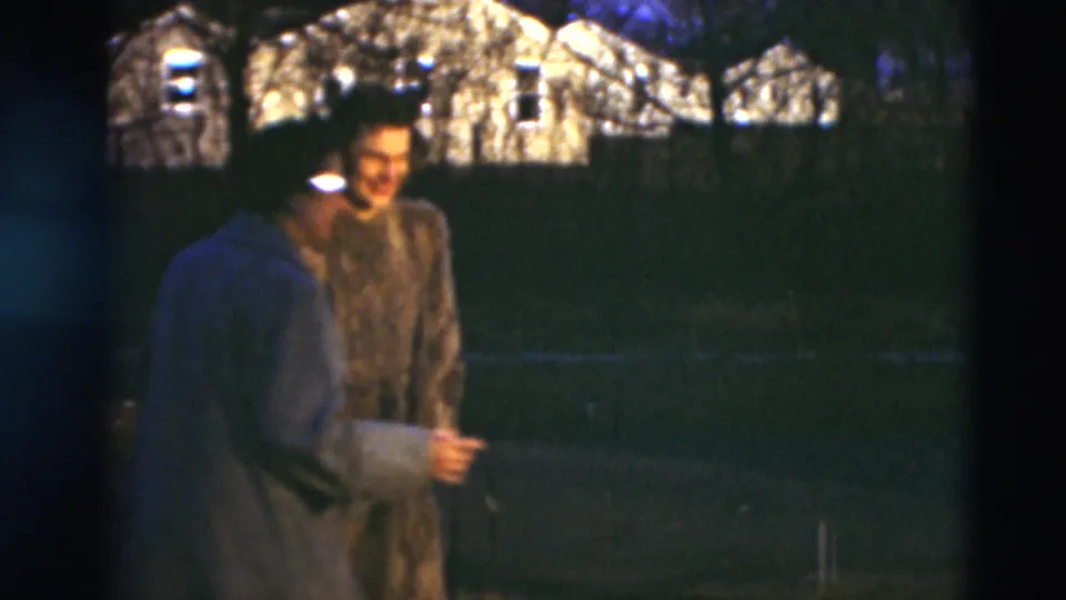 Two mature women in coats stand near a grassy area in Paducah, Kentucky, with bright houses and bare trees visible behind them.