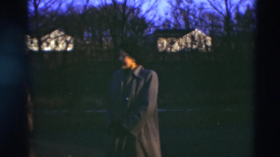 In Paducah, Kentucky home-movie footage from 1951, a woman in a long coat stands in a dark residential yard under a blue evening sky.