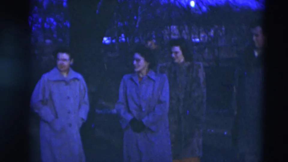 A small group of adults in long coats stands in a blue-toned Paducah yard at dusk, with trees and houses faintly visible behind them.