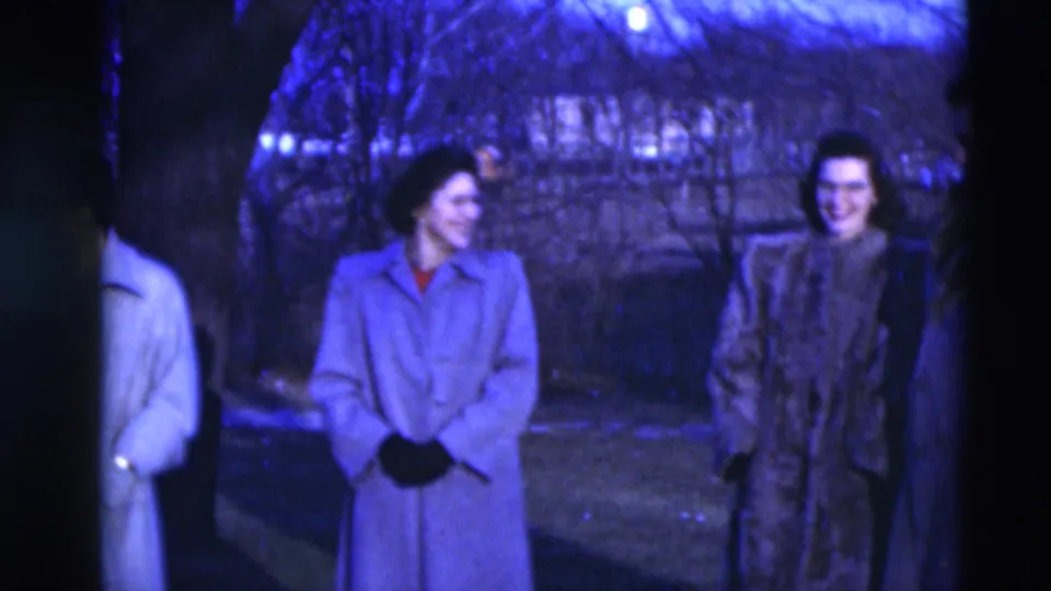 Two women in long coats appear to smile and talk outdoors in 1951 Paducah, with bare trees behind them.