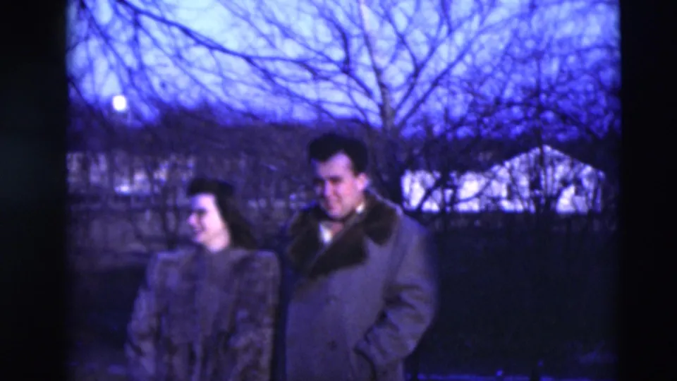 A woman in a textured coat and a man in a fur-collared overcoat stand outdoors in blue-tinted 1951 Paducah home-movie footage.