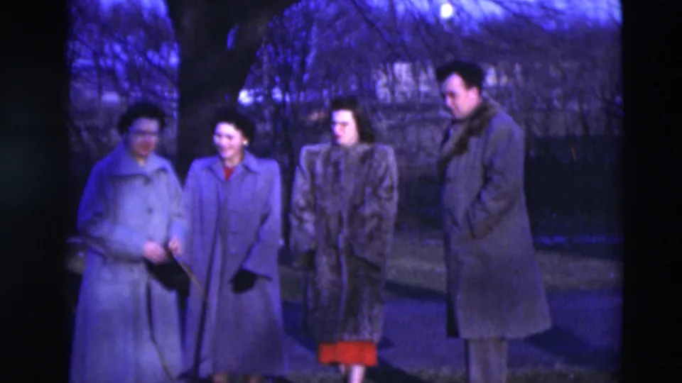 Four adults in 1951 Paducah, Kentucky home-movie footage gather outdoors in winter coats, with bare trees and grass visible at dusk.