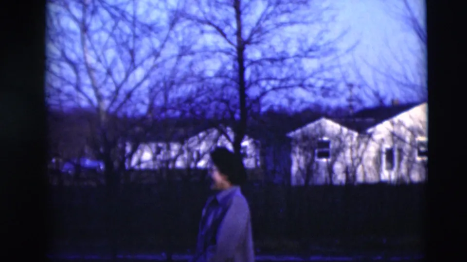 In 1951 Paducah, Kentucky footage, a woman walks through a shadowed yard before bare trees and modest houses.