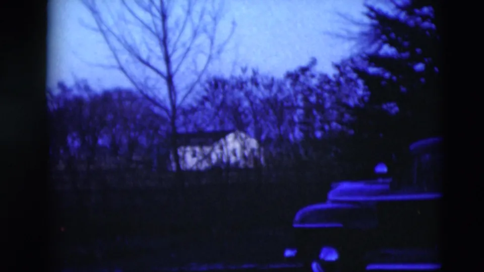 A blue-tinted residential view shows bare trees, distant houses, and part of a parked car in 1951 Paducah footage.
