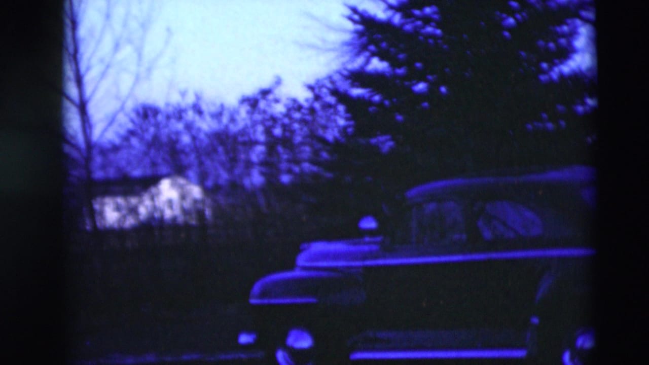 The pan reveals more of the parked car's side profile against trees and a house in the 1951 Paducah residential scene.