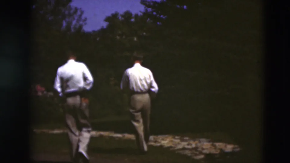 Two adult men walk away along a stone path in a wooded Paducah, Kentucky, setting captured on 1951 8mm film.