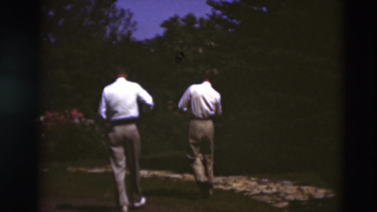 Two men in light shirts and trousers walk away on a garden path in 1951 Paducah, Kentucky home-movie footage.