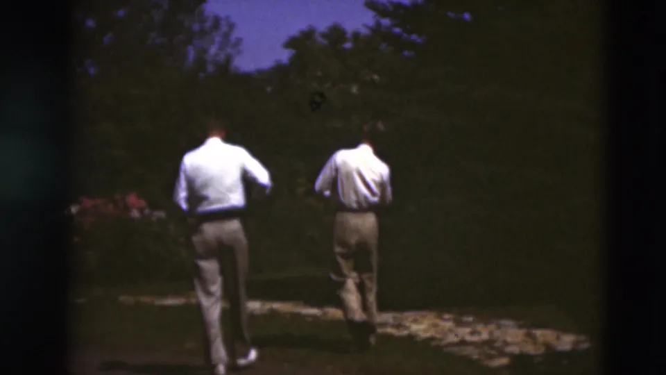 Two men in light shirts and trousers walk away on a garden path in 1951 Paducah, Kentucky home-movie footage.