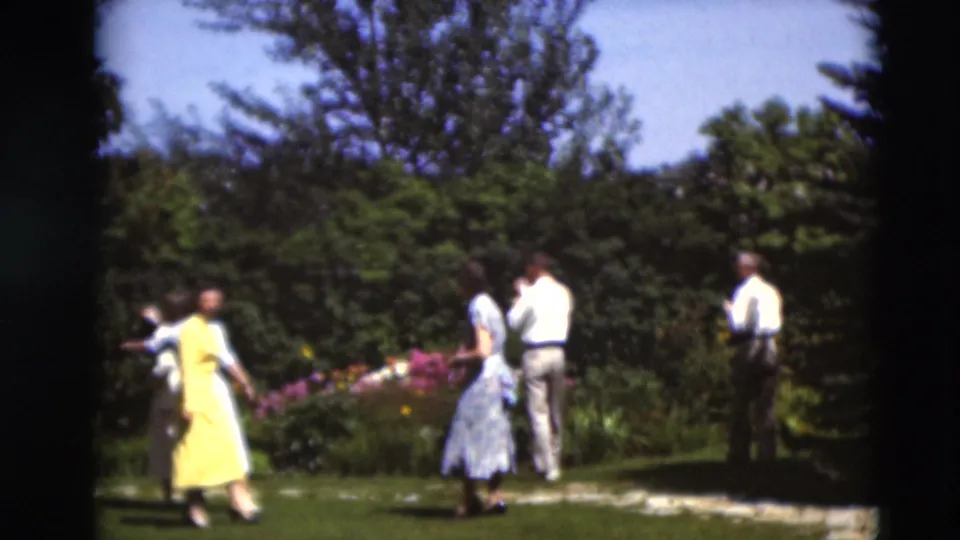 Women in yellow and blue dresses and men in light shirts walk through a landscaped garden in 1951 Paducah, Kentucky footage.