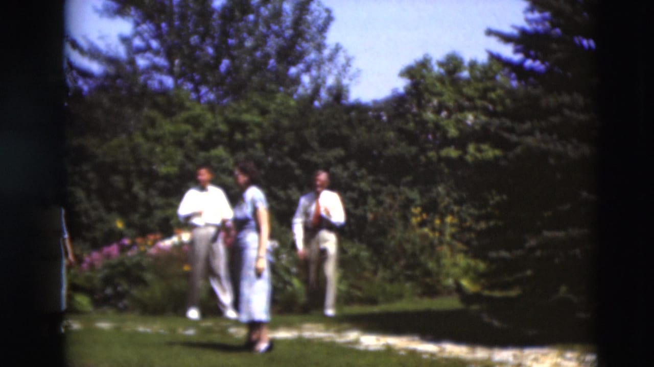 Three adults in formal summer clothing move through a bright Paducah garden in 1951 8mm footage.