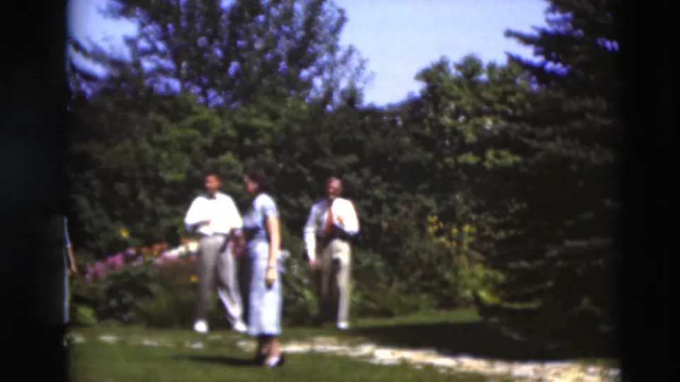 Three adults in formal summer clothing move through a bright Paducah garden in 1951 8mm footage.