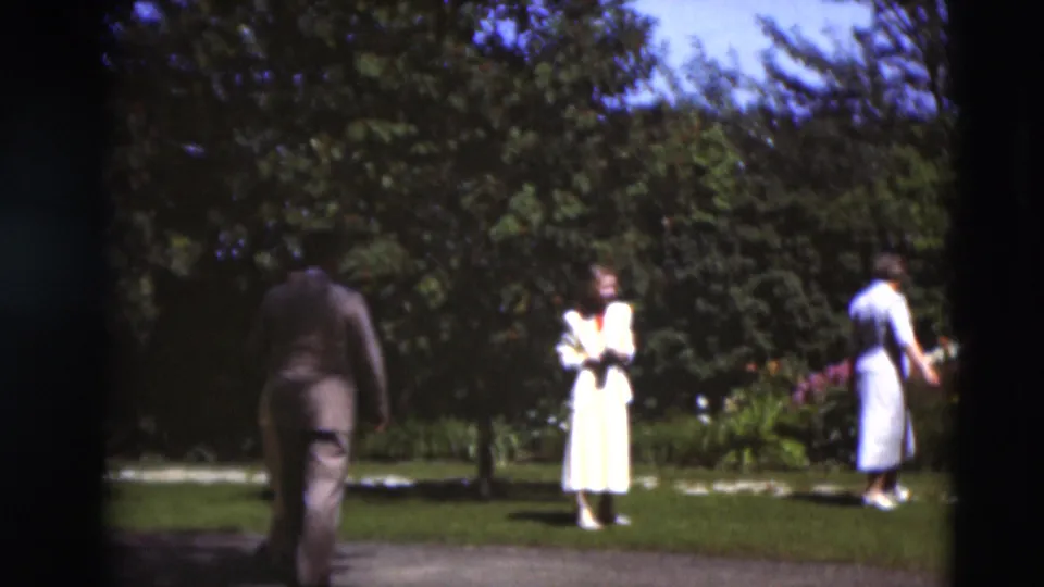 Adults in Sunday-best clothing move across a landscaped Paducah garden, with a woman in a light dress standing in view.
