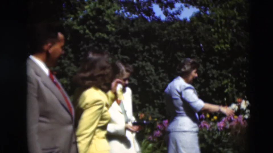 Mid-century adults in a Paducah garden, with a suited man and women watching as another woman reaches toward the blooms.