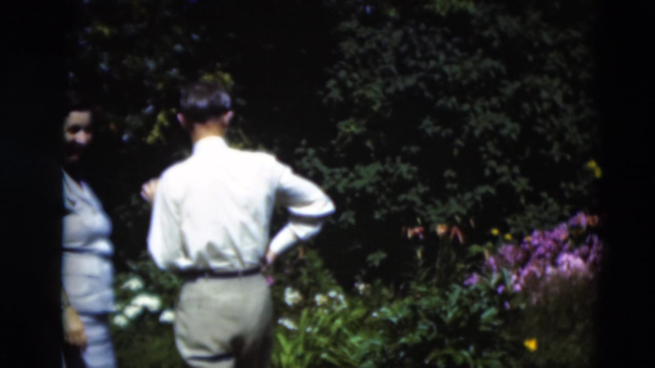 In 1951 Paducah home-movie footage, adults stand in a garden with purple blooms, green foliage, and bright sunlight filtering through shade.
