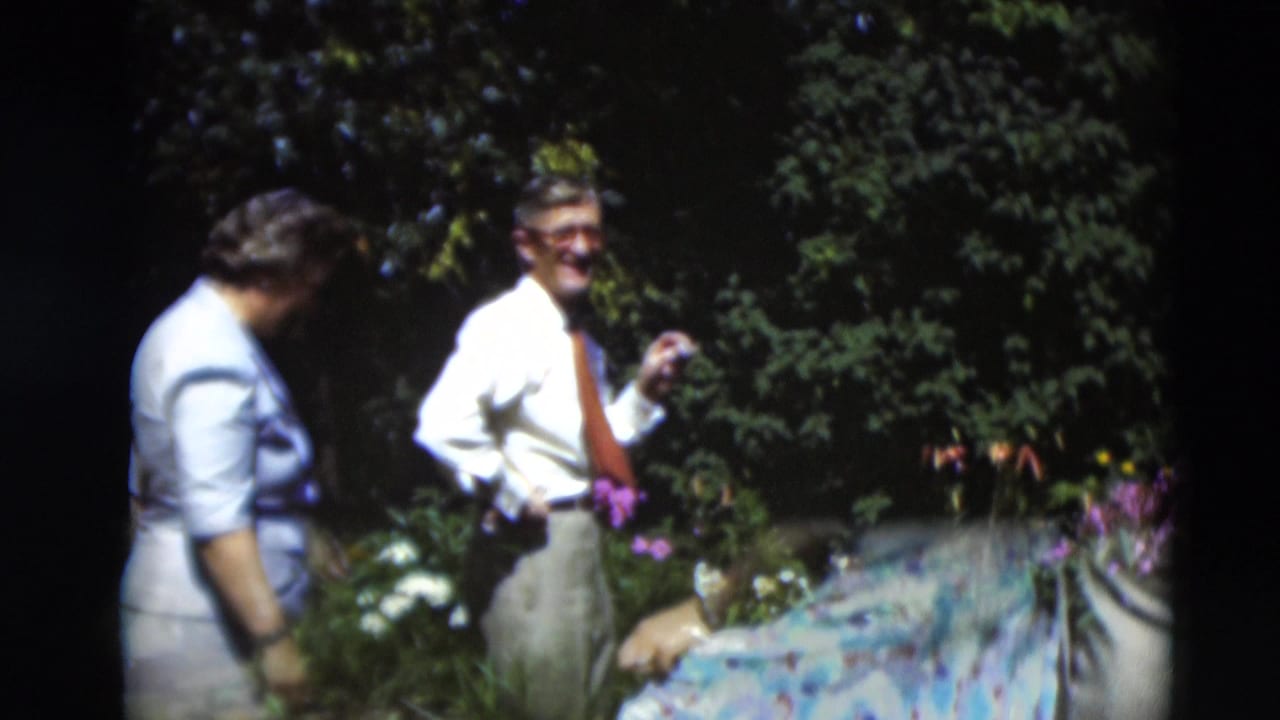 A woman in a light dress bends near garden flowers as a man in a white shirt and tie smiles in the 1951 Paducah home-movie scene.
