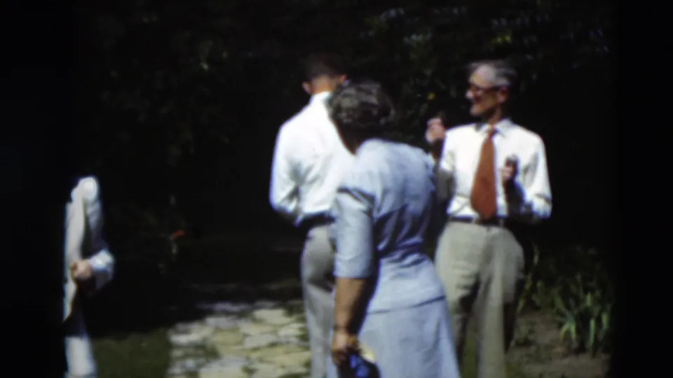 Three adults stand in the garden in 1951 Paducah footage, with a man in a white shirt and tie facing two others near foliage and flowers.