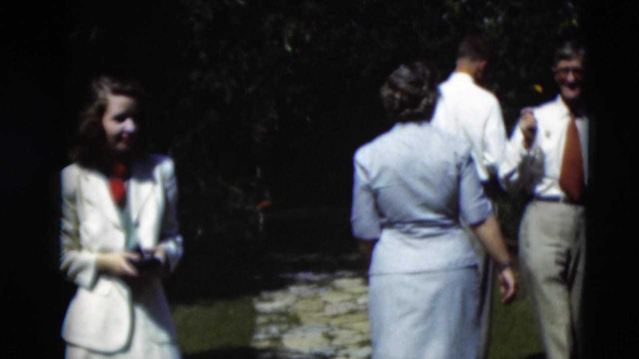 In 1951 Paducah home-movie footage, a woman in a white suit stands near adults conversing beside a stone garden path.