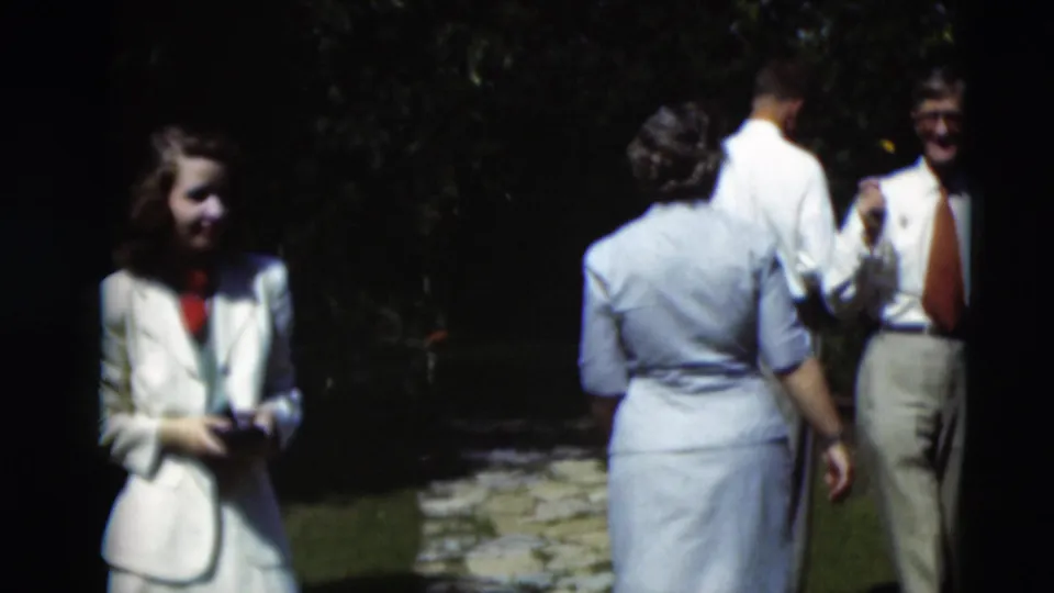 In 1951 Paducah home-movie footage, a woman in a white suit stands near adults conversing beside a stone garden path.