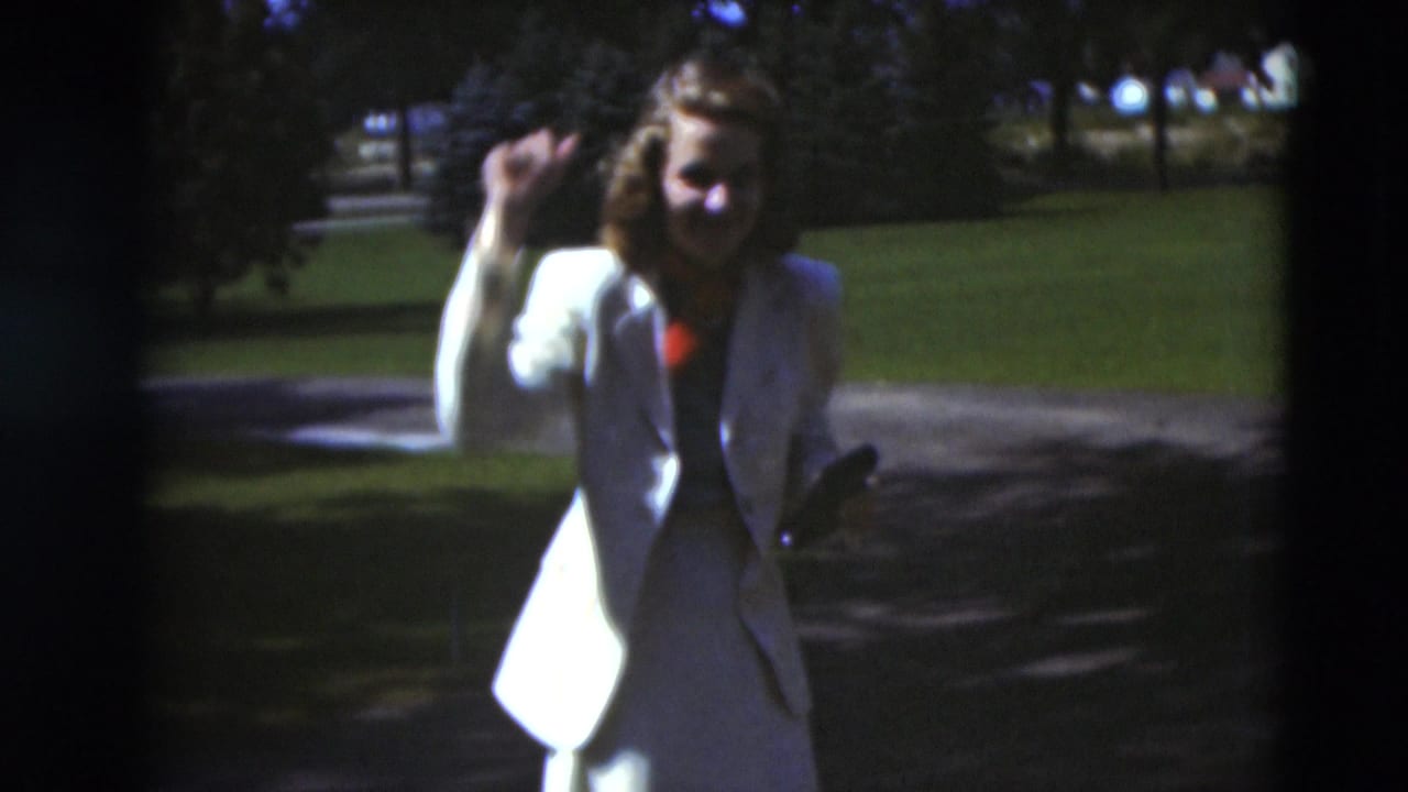In Paducah, Kentucky, a woman in a light suit raises her hand while standing outdoors on a sunny residential path in 1951 home-movie footage.