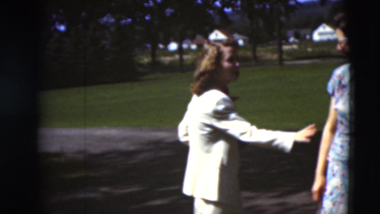 A woman in a light-colored suit reaches toward a friend in a floral dress on a sunny path in Paducah, Kentucky, in 1951.