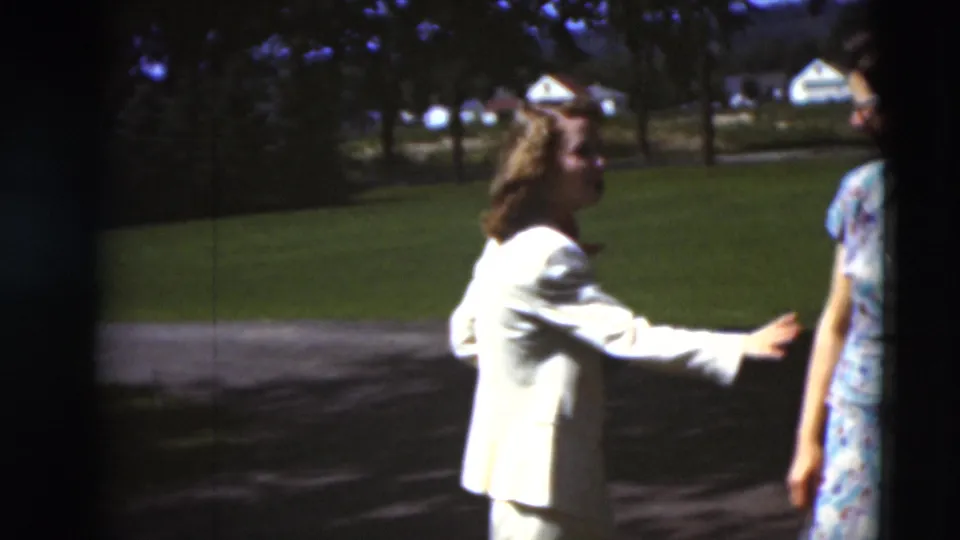 A woman in a light-colored suit reaches toward a friend in a floral dress on a sunny path in Paducah, Kentucky, in 1951.
