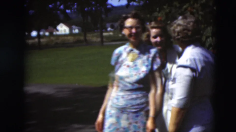 Three adults pose closely outdoors in Paducah, Kentucky, with trees, grass, and houses behind them in 1951 home-movie footage.
