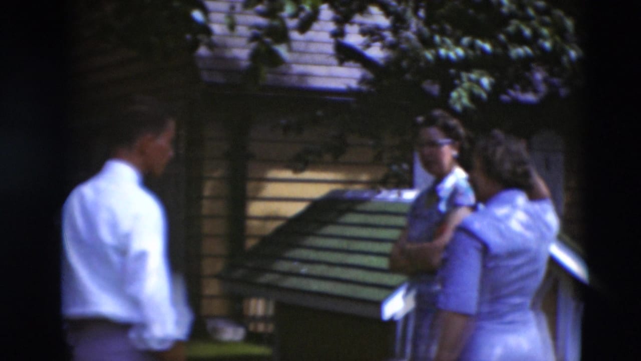 Adults standing in a shaded backyard near a small wooden structure and fence.