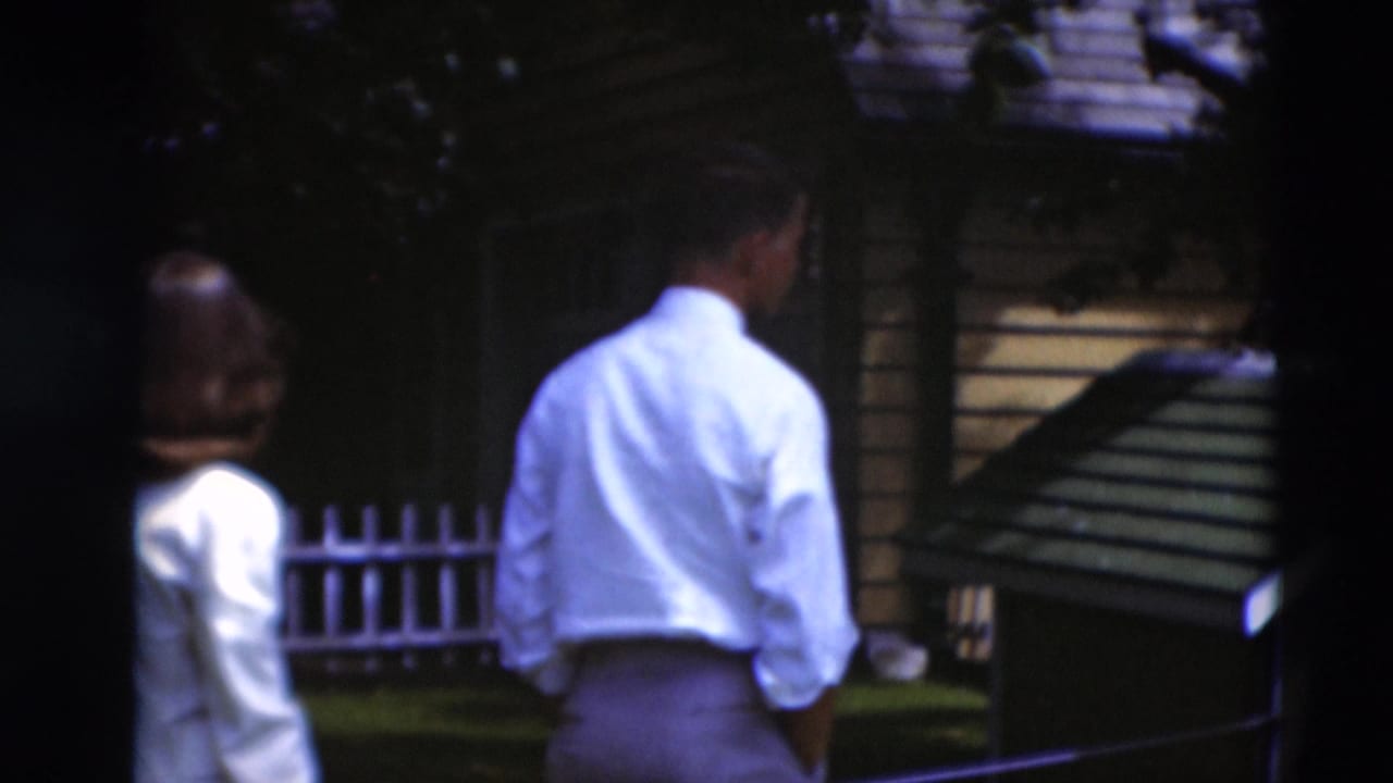 1951 Paducah backyard view with adults near a small wooden structure and a white picket fence.