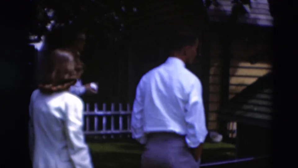 1951 Paducah frame showing adults from behind in a shaded backyard with fence and playhouse-like structure.