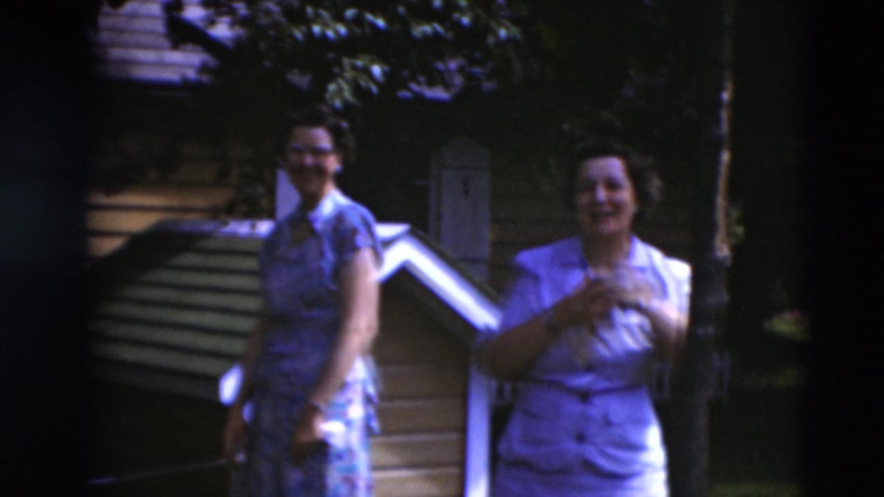 Two women in mid-century dresses stand near backyard steps and a small wooden structure in 1951 Paducah home-movie footage.