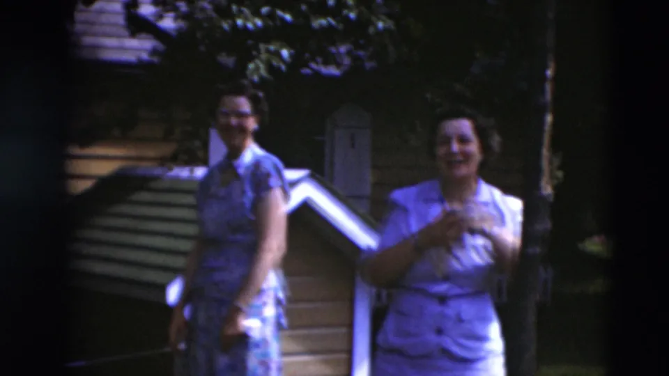 Two women in mid-century dresses stand near backyard steps and a small wooden structure in 1951 Paducah home-movie footage.