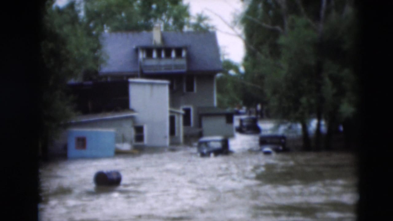 Paducah, Kentucky flood footage from 1951 showing muddy water around homes, trees, parked cars, and a blue shed.